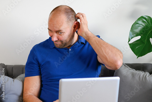 Man using laptop on sofa thinking