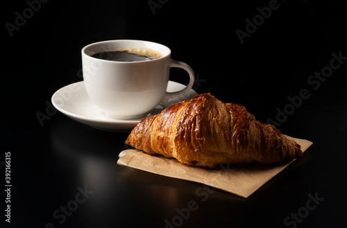 A croissant and hot coffee on a black background