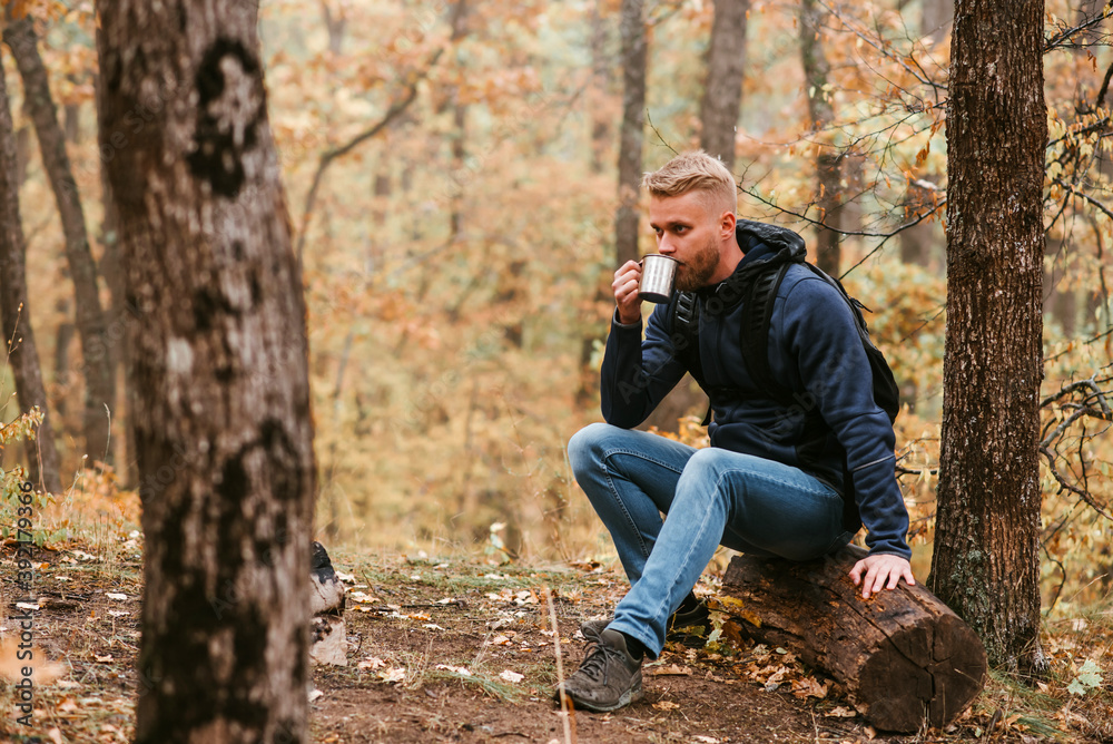 Guy traveler in the autumn forest rests on a halt and drinks tea. Guy traveler in the autumn forest rests on a halt and drinks tea.