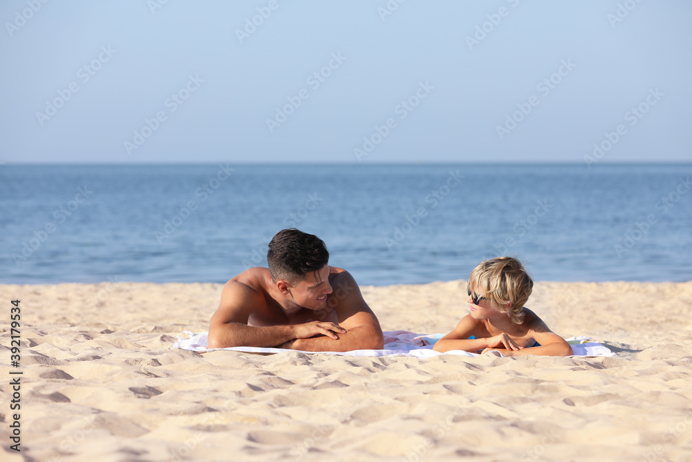 Father and son lying on sandy beach near sea. Summer holidays with family Father and son lying on sandy beach near sea. Summer holidays with family