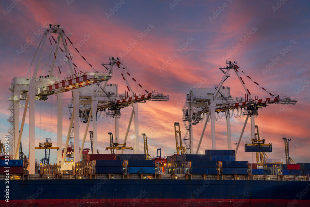 View of container cargo ship and crane bridge in shipyard at sunrise