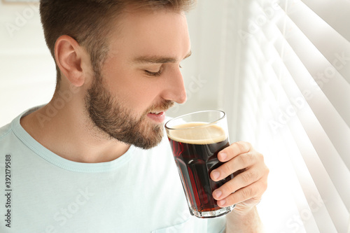 Handsome man with cold kvass indoors. Traditional Russian summer drink