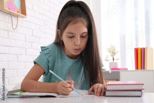 Pretty preteen girl doing homework at table