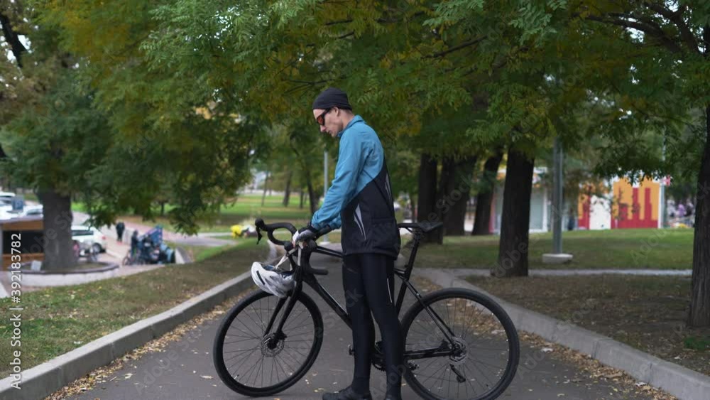 A young man stands near the bike, takes off his helmet from his head and hangs it on the handlebars. active lifestyle concept A young man stands near the bike, takes off his helmet from his head and hangs it on the handlebars. active lifestyle concept