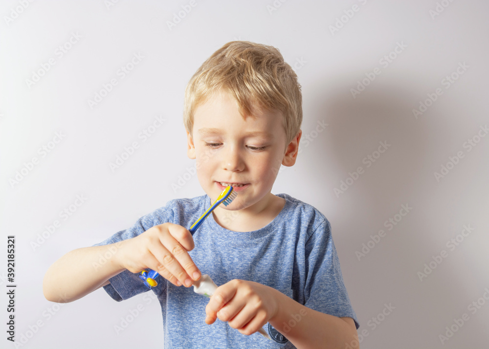 a boy with white hair holds a brush in his hands and squeezes the paste out of the tube onto the brush. Gray background. a boy with white hair holds a brush in his hands and squeezes the paste out of the tube onto the brush. Gray background.