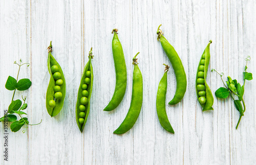 Pods of green peas with pea leaves on a white wooden background. Organic food.