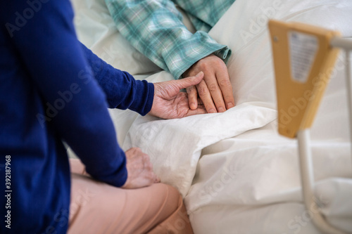 入院中の夫の手を握る妻 © Monet