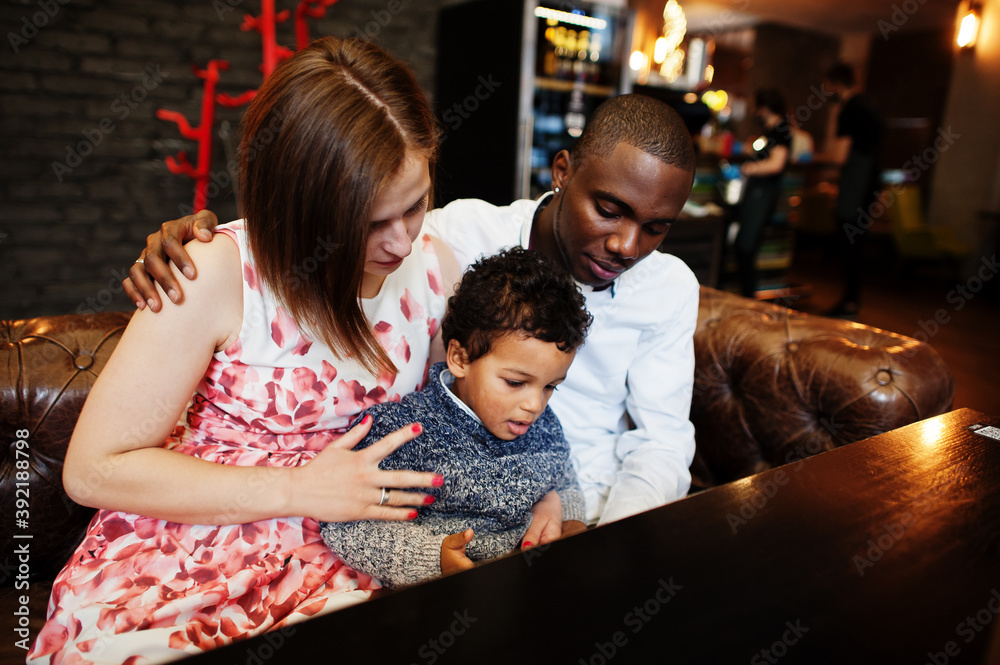 Happy multiethnic family with boy kid spend time at restaurant. Relationships of african man and white european woman.
