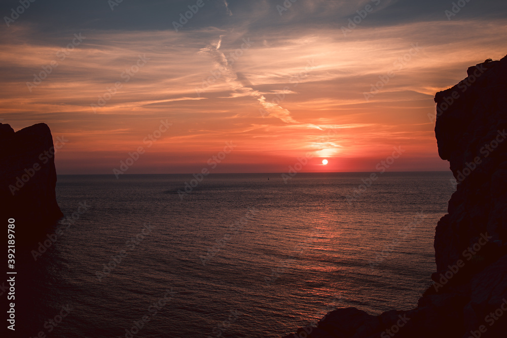 Beautiful and scenic sunset on the rocks in the famous lokking point of CAPO CACCIA, in Sardinia, one of Italy's main Islands. Sun going down above water, beautiful orange sky.