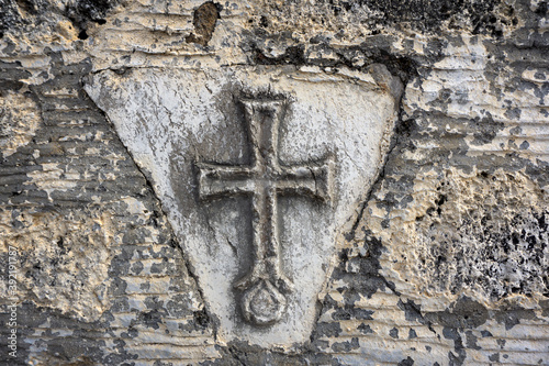 Ancient Greek Christian cross on the old stone wall of the temple.
