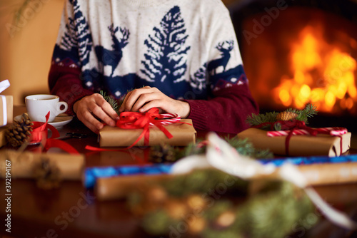  Men's hands hold Christmas present. Man using red ribbon, green fir tree twig to create Christmas gift. Wintar holiday. 