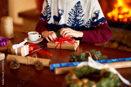  Men's hands hold Christmas present. Man using red ribbon, green fir tree twig to create Christmas gift. Wintar holiday. 