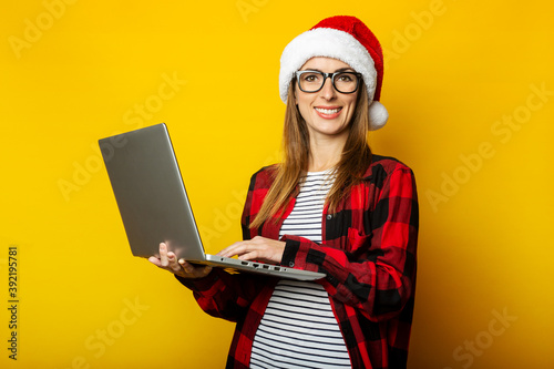 Wallpaper Mural Young woman with a smile in a santa hat and a red shirt in a cage holds a laptop in her hands on a yellow background Torontodigital.ca