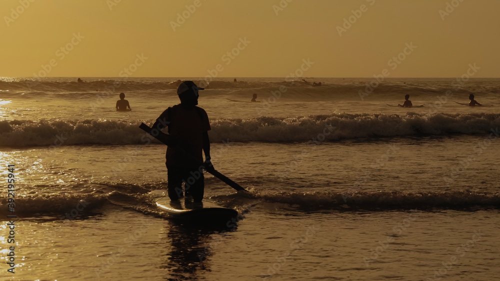 young guy riding a surf with a paddle at sunset