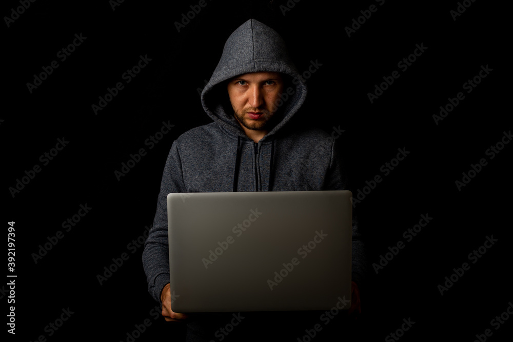 Man in a hood holds a laptop in his hands on a dark background. Concept of cyber rogue, hacker. Banner Man in a hood holds a laptop in his hands on a dark background. Concept of cyber rogue, hacker. Banner