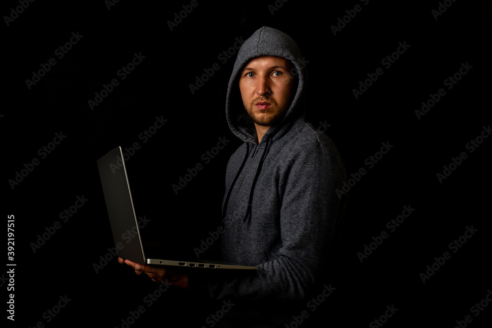 Man in a hood holds a laptop in his hands on a dark background. Concept of cyber rogue, hacker. Banner Man in a hood holds a laptop in his hands on a dark background. Concept of cyber rogue, hacker. Banner