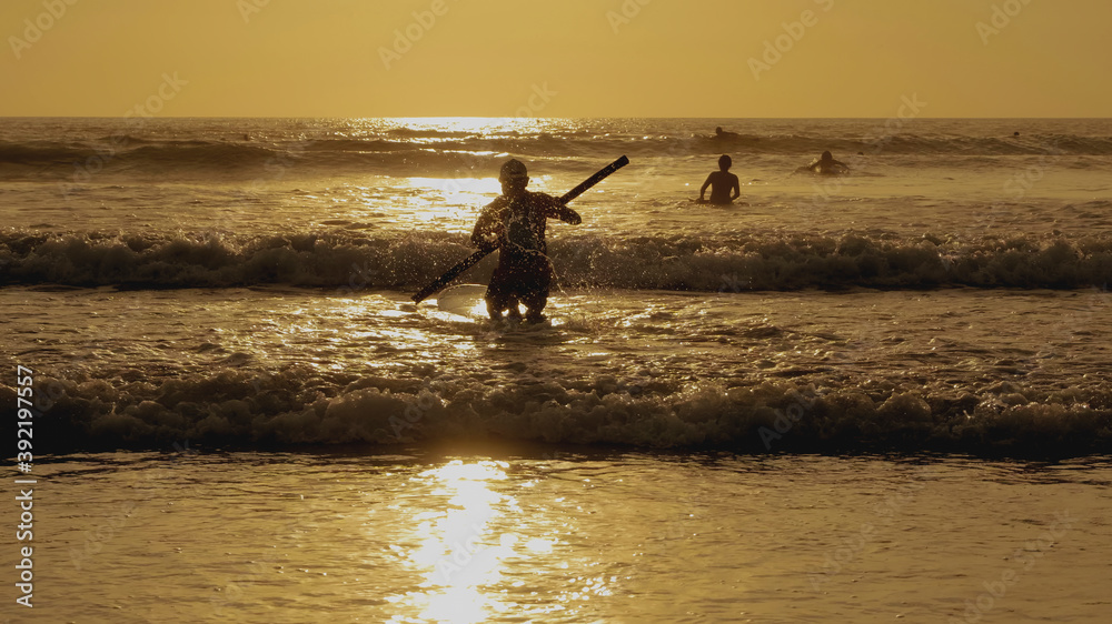 young guy riding a surf with a paddle at sunset