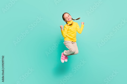 Full body photo of brown haired happy girl jump air lucky sale raise fists wear yellow jumper white pants isolated on teal color background