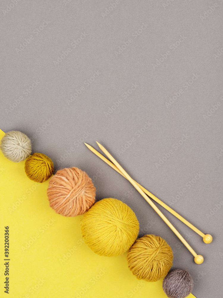 Row of various coloured clews of yarn and wooden knitting needles on gray and illuminating yellow background. Craft, knitting or handmade concept. Winter hobby background. Top view, flat lay. Row of various coloured clews of yarn and wooden knitting needles on gray and illuminating yellow background. Craft, knitting or handmade concept. Winter hobby background. Top view, flat lay.
