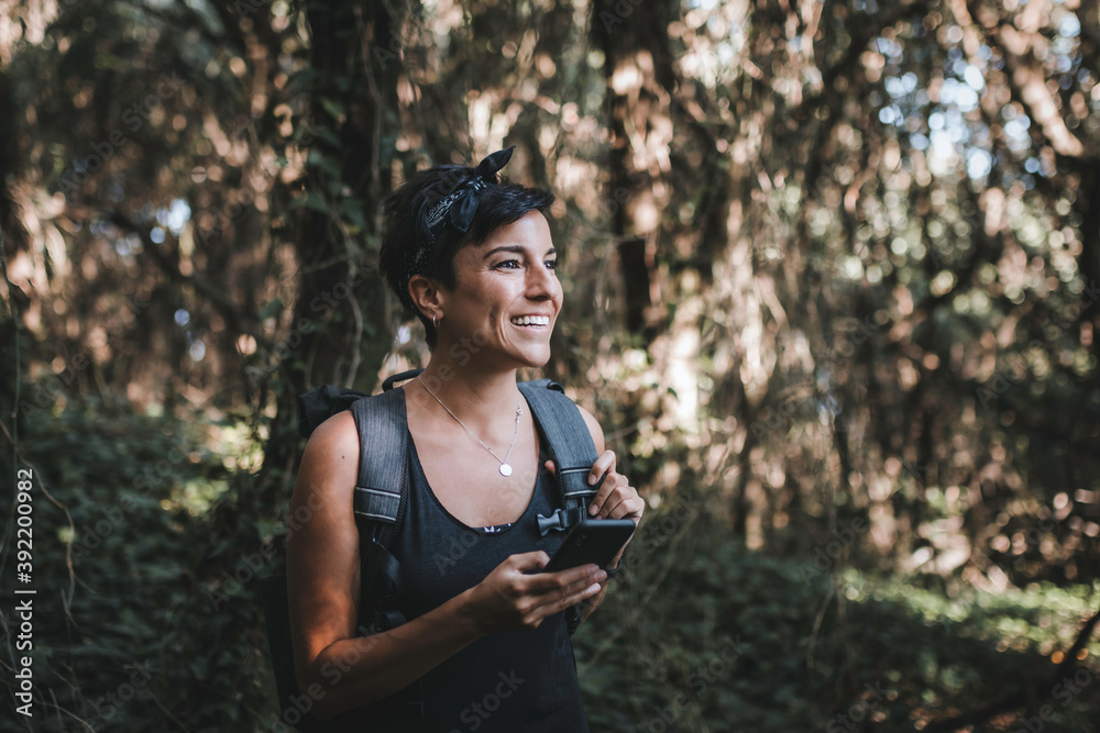 Woman holding her phone in the while hiking wearing a backpack Woman holding her phone in the while hiking wearing a backpack