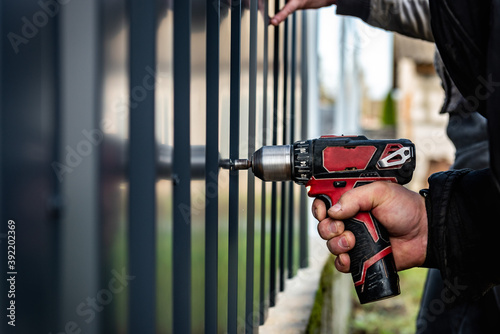 Metal fence installation. The worker is screwing the screw into the metal fence. photo