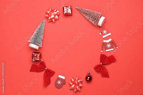 Christmas ornaments. Stocking, gifts, winter tree, ribbon and bow in shape frame on red background for greeting card. Flat lay, top view, copy space.