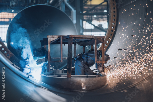 Workers cutting and welding steel tanks with flying sparks and dynamic light