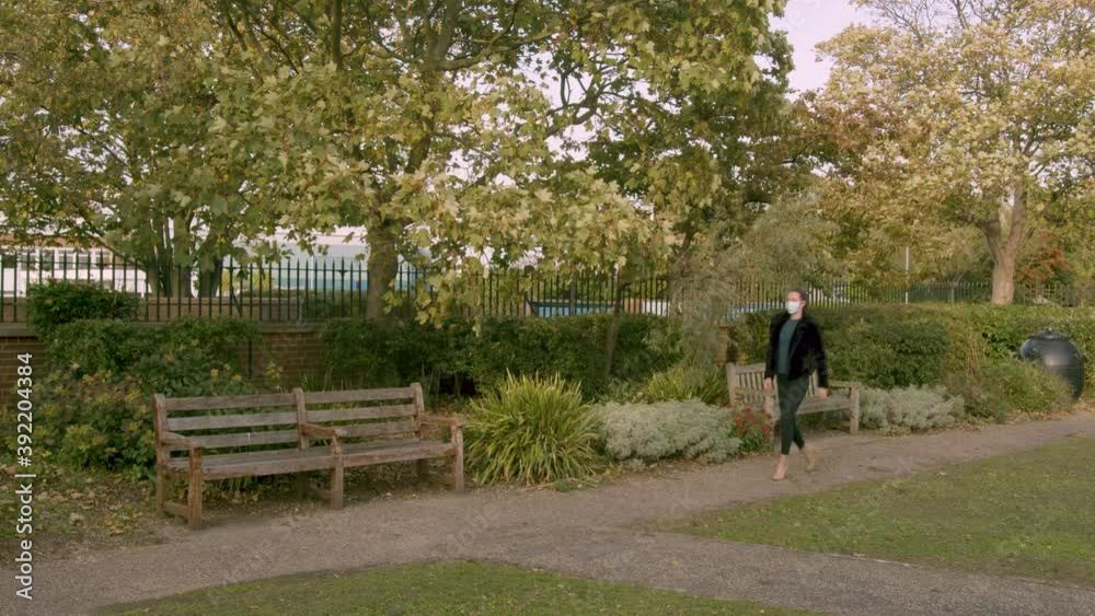 Female wearing a medial facemask whilst walking in a park Female wearing a medial facemask whilst walking in a park