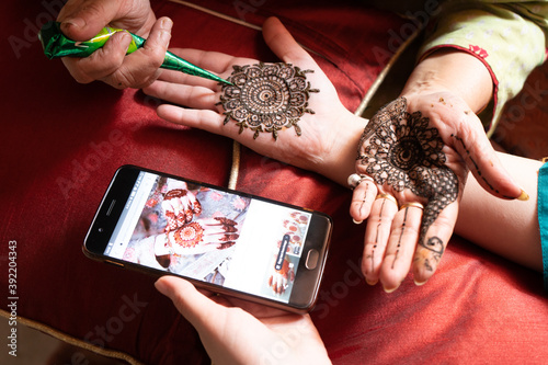 Woman getting a henna tattoo mehendi design copied from phone onto her hand for the bride bridesmaid shaadi event or a hindu festival like karwachauth diwali holi and teej photo