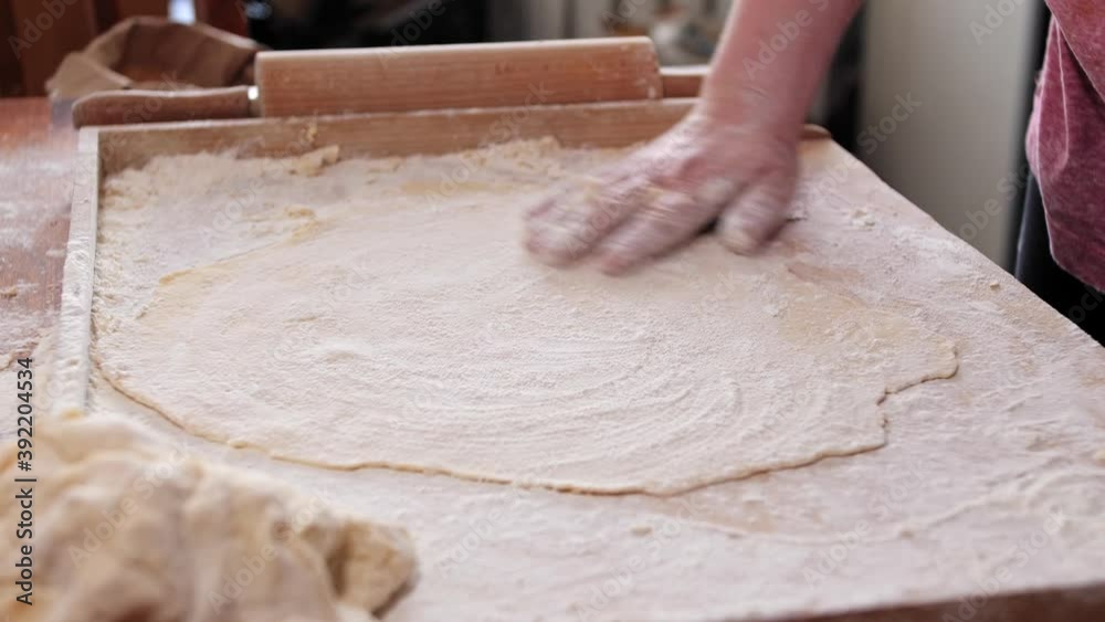Woman, housewife, sprinkles flour on the rolled dough. Rolls up the roll. Handmade noodles at home. Woman, housewife, sprinkles flour on the rolled dough. Rolls up the roll. Handmade noodles at home.