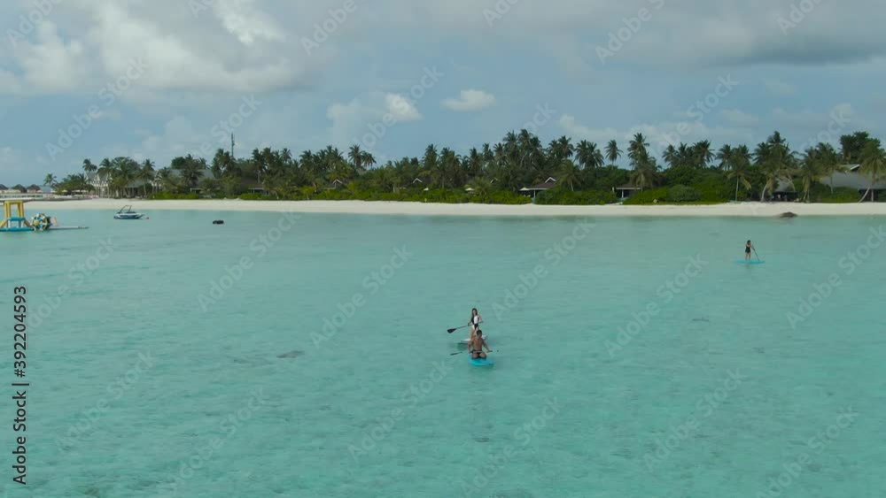 Couple paddle boarding together over clear blue sea with stunning resort Couple paddle boarding together over clear blue sea with stunning resort