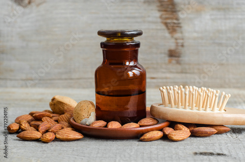 Pharmacy bottle with almond oil and wooden hair brush. Natural hair care concept. Old wooden background. Almonds close up. Copy space