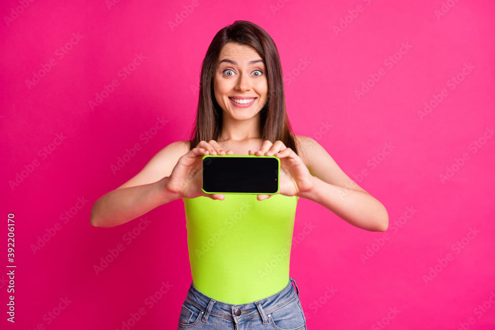Photo of charming excited girl hold telephone show screen empty space toothy smile wear green top isolated vivid pink color background Photo of charming excited girl hold telephone show screen empty space toothy smile wear green top isolated vivid pink color background