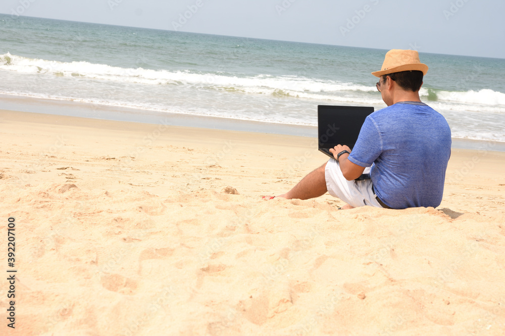 A man using his laptop and working from sea beach, during this pandemic where work from home is part of life , now people can work from anywhere and at the same time have a feel of vacation