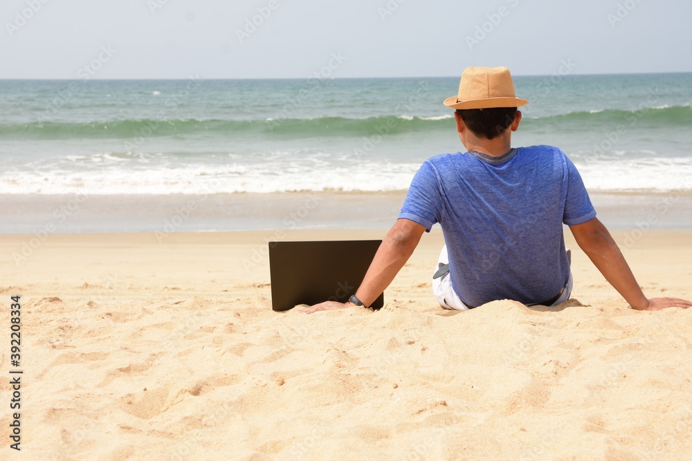 A man seating with his laptop and working from sea beach