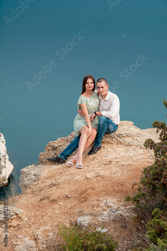 Young married couple admires the sea or ocean at edge of a rocky cliff. Family photoshoot on background of crag