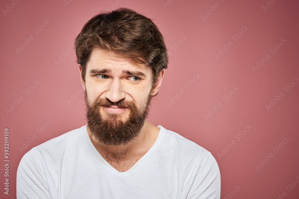 Emotional bearded man in white T-shirt discontent pink background Emotional bearded man in white T-shirt discontent pink background