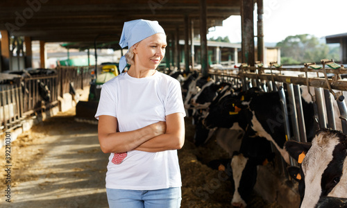 glad senior female farmer posing in cowshed at dairy farm