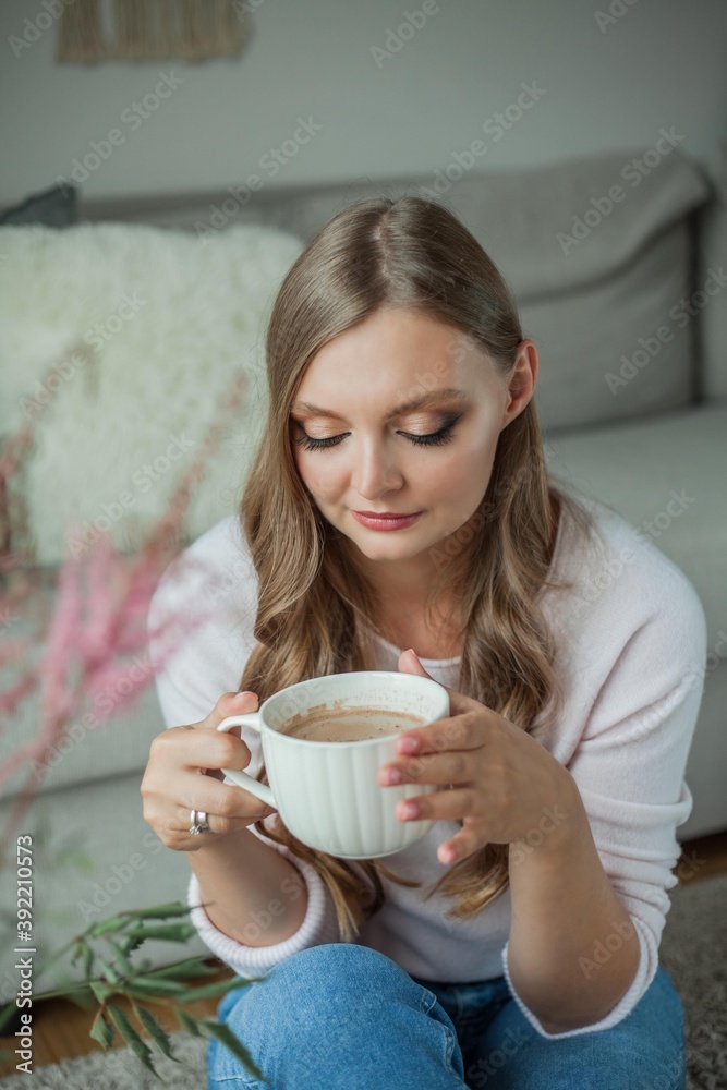 Beautiful young woman drinking hot cocoa and sitting by the window at home Beautiful young woman drinking hot cocoa and sitting by the window at home