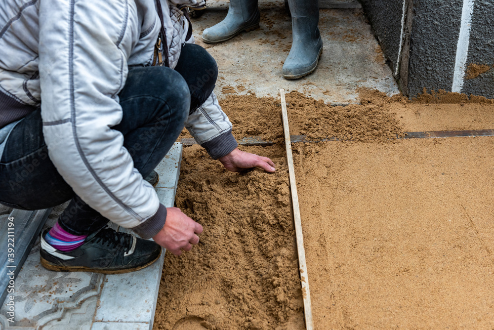 Worker screeding sand bedding to level for laying paving slabs. Worker screeding sand bedding to level for laying paving slabs.