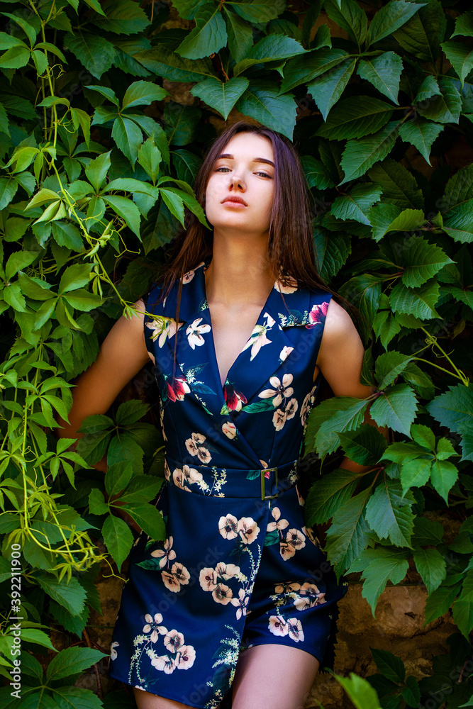 Young woman in blue flowers dress on green ivy background Young woman in blue flowers dress on green ivy background