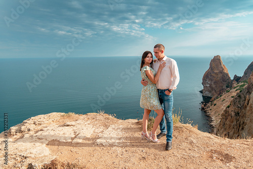 Young married couple admires the sea or ocean at edge of a rocky cliff. Family photoshoot on background of crag