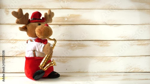 Stuffed reindeer playing saxophone and dancing on a white wooden wall celebrating christmas.