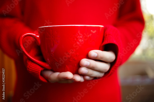 a large mug in the hands of a child on a red background