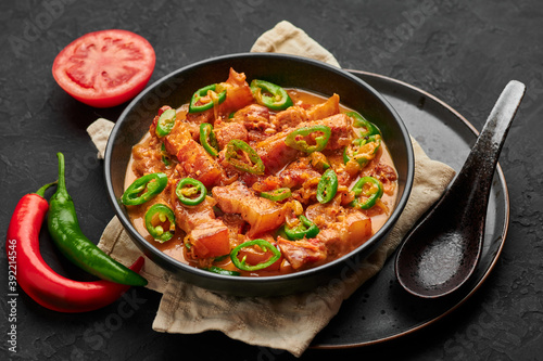 Bicol Express Stew in black bowl on dark slate table top. Filipino cuisine spicy pork belly coconut milk curry. Asian food.