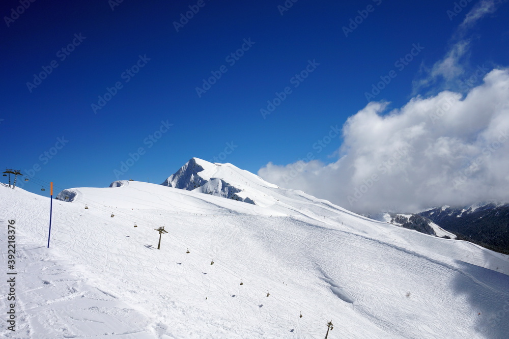 Obraz premium Winter landscape in the mountains. Snow-capped mountain peaks, blue sky, ski slopes.