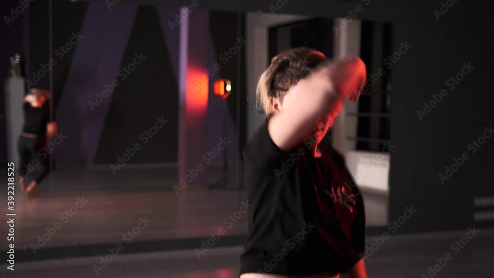 Cheerful young woman dancing modern dance with elements of vogue and strip plastic in choreography studio in front of a mirror. Slow motion.