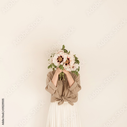 Young beautiful woman with white peonies flowers bouquet agains white wall.