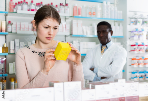 Pensive pleasant young woman choosing medicines in modern pharmacy photo