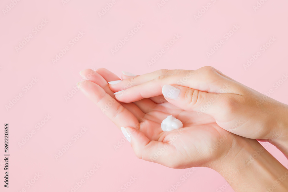 White moisturizing natural cream in young adult woman hand isolated on light pink background. Pastel color. Care about clean, soft and smooth body skin. Closeup. Side view. White moisturizing natural cream in young adult woman hand isolated on light pink background. Pastel color. Care about clean, soft and smooth body skin. Closeup. Side view.
